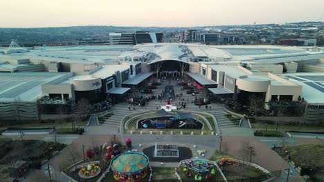 Retreating-ascending-drone-shot-of-the-Mall-of-Africa-Shopping-Center-from-the-Town-Square-entrance,-Midrand,-South-Africa