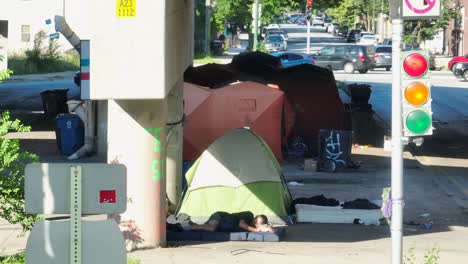 Homeless-man-sleeping-under-highway-overpass-in-community-of-tents