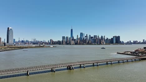 Aerial-flight-over-hudson-river-in-New-York-City-with-beautiful-skyline-and-one-world-trade-center-in-background-during-sunny-day-with-blue-sky---Goldman-Sachs-Tower-on-the-left-in-Jersey-City