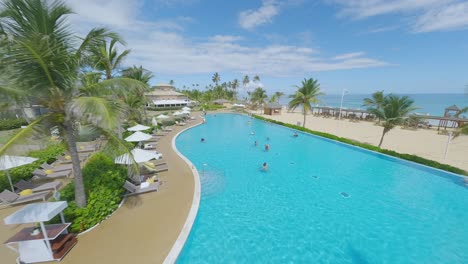 Drone-flight-over-large-swimming-pool-with-resting-and-cooling-Tourist-at-NICKELODEON-RESORT,-PUNTA-CANA-in-Summer
