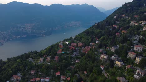 Video-Aéreo-De-Drones-De-Casas-En-Una-Colina-Con-El-Lago-Como-Y-Montañas-Al-Fondo