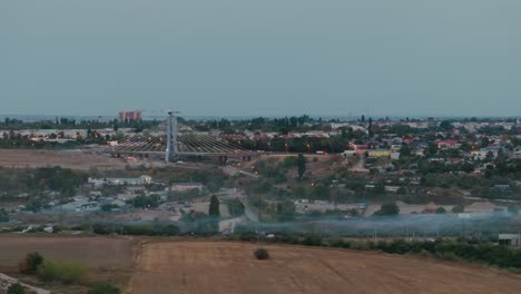 Drone-shot-with-the-construction-site-of-a-suspended-bridge,-city-lights-and-a-mysterious-blanket-of-smoke-or-fog-settles-4K50Fps