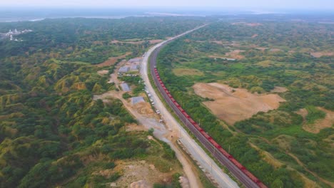 Aerial-Drone-shot-of-a-Freight-train-moving-through-semi-arid-forest-valley-of-Chambal-river-in-India