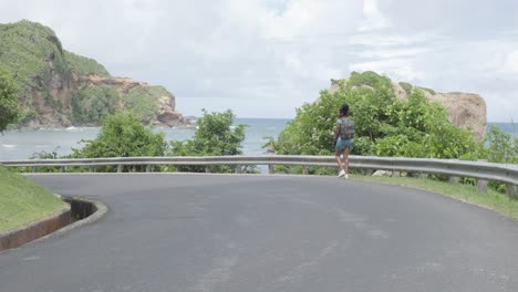 Frau-Im-Kleid-Geht-Entlang-Einer-Straße-Mit-Meerblick-In-Calibishie,-Dominica