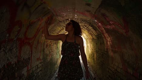Caucasian-girl-in-a-green-floral-dress-walks-in-a-tunnel-at-sunset,-medium-shot