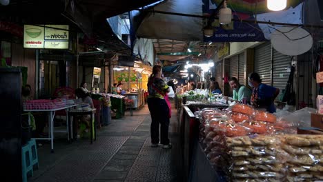 Sidewalk-vendors-making-a-negotiation-of-the-price-with-a-customer,-Amphawa-Night-Market,-Thailand