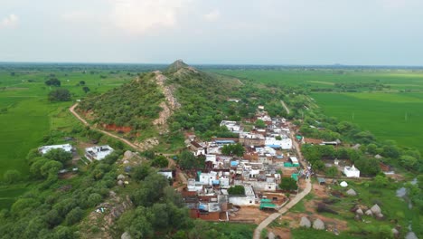 Aerial-drone-shot-of-a-village-under-a-green-hill-with-paddy-fields-all-around-at-a-small-village-in-ndia