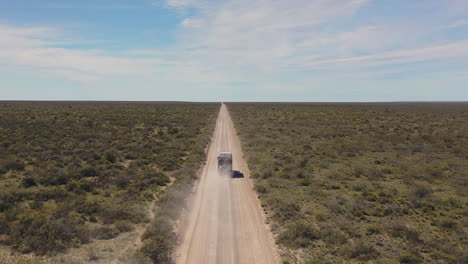 Truck-driving-alone-straight-desert-road,-dust,-drone-footage