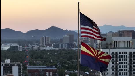 Phoenix-skyline-stands-against-a-mountain-backdrop,-while-the-American-and-Arizona-flags-proudly-fly