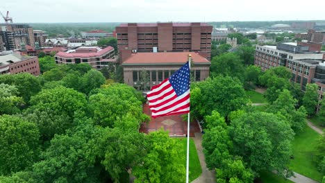 Aerial-orbit-around-waving-American-flag-on-University-of-Michigan-campus-on-rainy-summer-day