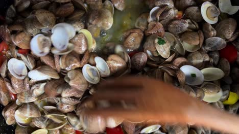 Stirring-delicious-fresh-shell-clams-with-parsley-peppers-and-tomatoes-with-wooden-forks-in-hot-pan