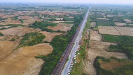 Aerial-Drone-shot-of-a-Freight-train-moving-through-farmlands-in-Morena-India