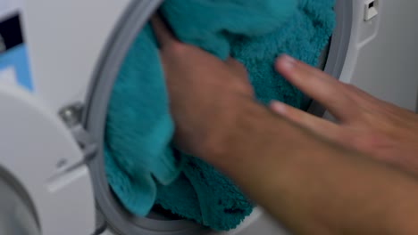 Close-up-slow-motion-hands-placing-cotton-towels-into-front-loader-washing-machine-cleaning-detergent-laundry-household-chore-4K