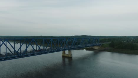 Aerial-establishing-view-of-the-steel-bridge-over-Lielupe-river-on-a-sunny-summer-morning,-fog-rising-over-the-river,-cars-driving,-wide-ascending-drone-shot-moving-forward