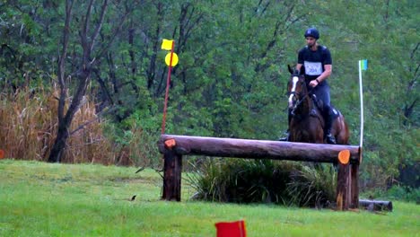 Ein-Pferd-Mit-Reiter-Springt-Bei-Starkem-Regen-Bei-Einem-Cross-Country-Wettbewerb-über-Ein-Hindernis