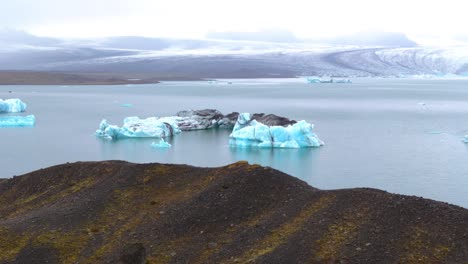 Vista-Aérea-Panorámica-De-Un-Iceberg-En-Un-Lago-Glaciar-En-Islandia,-Rodeado-De-Montañas-Nevadas
