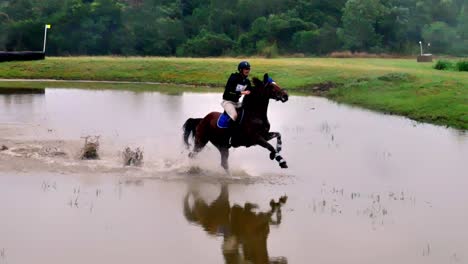 Close-up-shot-of-horse-and-its-rider-galloping-through-a-water-pool
