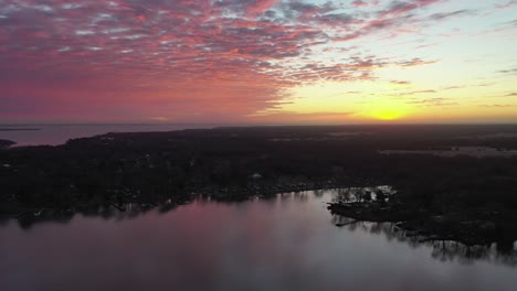 Aerial-hyperlapse-above-pier-as-red-pink-clouds-glow-above-the-lake-coastline