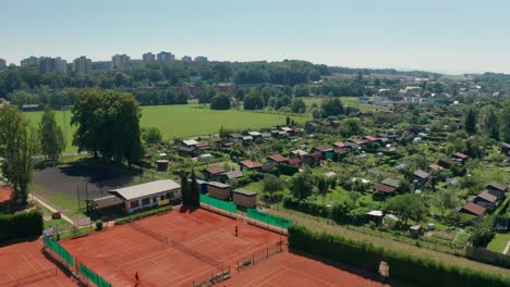 Aerial-drone-shot-of-sunny-day-in-gardening-colony-with-tennis-court,-cabins,-huts-and-shacks-in-the-middle-of-city