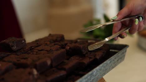 Hand-with-Tongs-Picking-up-Chocolate-Brownie-at-Party,-Close-up
