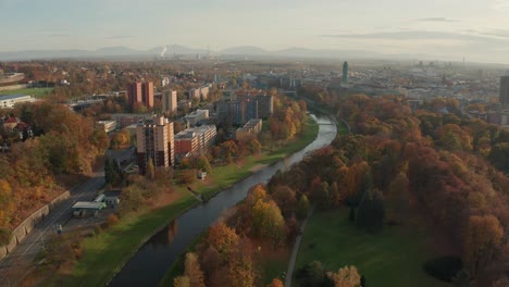 Aerial-drone-shot-of-a-czech-big-city-Ostrava-with-alongside-river-buldings,-cars,-roads,-apartments,-power-plant-and-towers-during-autumn-fall-day