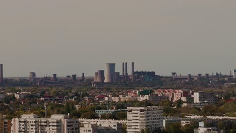 High-zoom-drone-shot-tracking-an-expansive-industrial-area,-revealing-a-lot-of-towering-smokestacks-over-the-city-skyline-4K60Fps