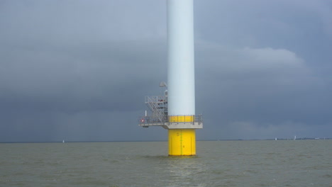 Sailing-close-to-the-bottom-of-a-large-wind-turbine-of-a-near-shore-wind-farm-on-a-fresh-water-lake