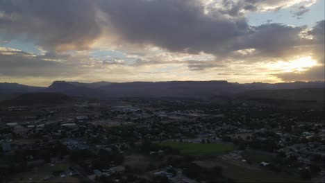 A-slow-drone-pullout-shot-over-a-small-village-out-west-with-a-majestic-sunrise-and-beautiful-clouds-backlighting-the-mountains