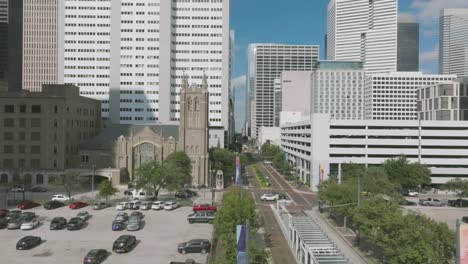 An-aerial-establishing-shot-of-Main-Street-zooming-out-with-a-Metro-Train-traveling-south-on-a-sunny-day-with-white-clouds-in-downtown-Houston-Texas
