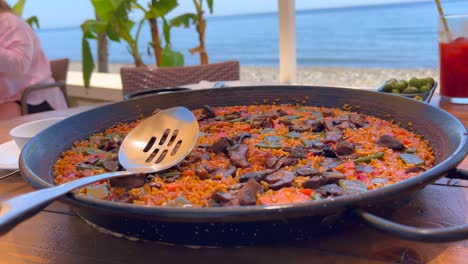 Traditional-Spanish-Paella-dish-with-vegetables-in-a-restaurant-by-the-sea,-tasty-cooked-rice-with-vegetables,-green-olives-tapas,-Marbella-Spain,-4K-shot