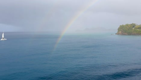 Blick-Auf-Den-Doppelten-Regenbogen-über-Dem-Wasser,-Während-Das-Segelboot-Von-Links-Einfährt