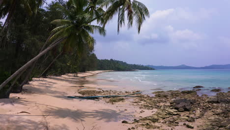 Palm-trees-along-white-sand-beach-washed-by-ocean-waves,-Koh-Kood