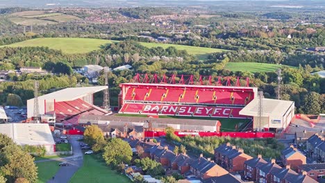 Drone-descends-above-Barnsley-Football-club-soccer-stadium-or-pitch,-vibrant-red-seats