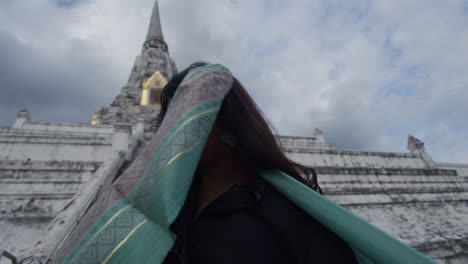 woman-covering-her-face-in-the-Buddhist-temple-Wat-Arun,-Temple-of-Dawn,-holding-a-scarf,-which-is-located-on-the-banks-of-the-Chao-Phraya-River