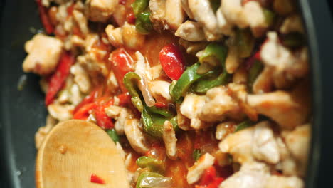 Wooden-spoon-stirring-chicken,-vegetable-fajita-mix-in-skillet-vertical-close-up