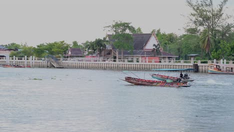 Touring-boat-stopping-in-the-middle-of-the-river-as-another-long-boat-moves-going-to-the-left-at-a-river-in-Amphawa-in-Samaut-Songkhram,-Thailand