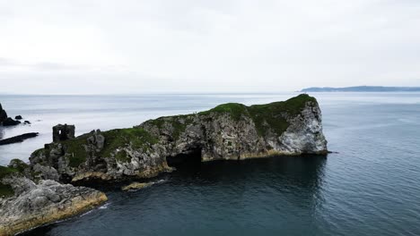 Aerial-view-of-the-majestic-Kibane-Castle-in-Northern-Ireland,-taken-along-the-mighty-coastal-causeway-overlooking-the-calm-sea,-rocks-and-an-island-in-the-background-during-an-expedition