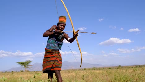 Portrait-Of-A-Karamojong-Hunter-Shooting-An-Arrow-While-Hunting-Pangolin-In-Uganda,-Africa