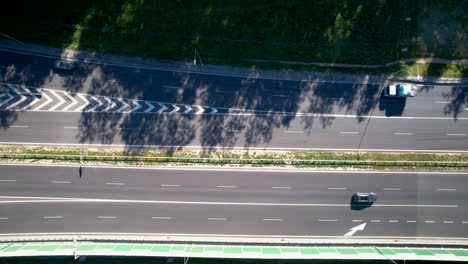 Top-down-shot-of-vehicles-on-a-sunlit-road-with-tree-shadows-and-pedestrian-crossings