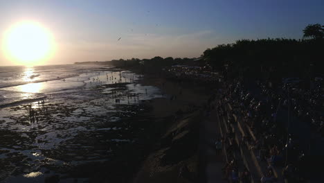 People-sitting-on-stairs-and-walking-on-Canggu-beach,-watching-sunset