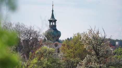 A-church-spire-with-a-patina-covered-roof-towers-above-the-blooming-spring-orchard