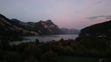 A-beautiful-pink-sky-overlooks-the-epic-lake-of-Walensee,-surrounded-by-mountain-Alps