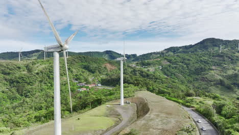 Aerial-footage-of-elongated-white-wind-turbines-atop-rolling-hills,-capturing-the-beauty-of-green-energy-in-motion