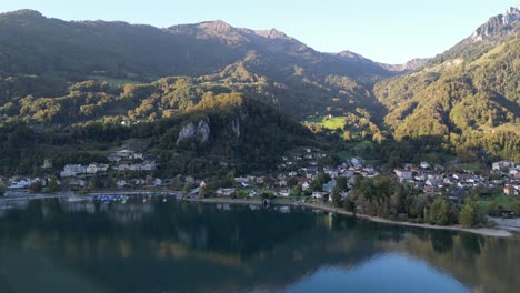 An-aerial-view-above-Walensee-captures-a-small-marina-and-residential-houses-with-the-majestic-green-dressed-mountain-Alps-reflected-beautifully-in-the-water-on-a-sunny-day
