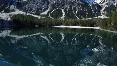 Snow-covered-mountain-peaks-towering-over-a-serene-alpine-lake-surrounded-by-dense-forest