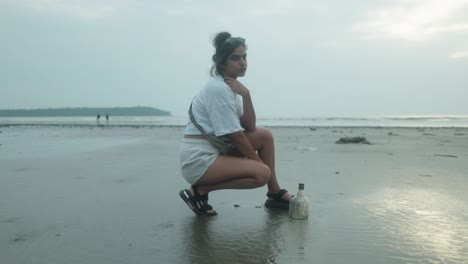 A-young-girl,-crouched-on-the-beach,-looks-directly-at-the-camera
