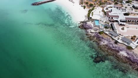 Aerial-view-of-a-tourist-paradise-on-the-coast-of-Playa-El-Caymancito-near-La-paz-Baja-California-Sur,-Mexico-overlooking-the-beautiful-beach-and-turquoise-sea-with-hots-and-dry-landscape-in-summer