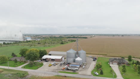 Grain-Silos,-Barns,-and-a-Natural-Gas-Power-Plant-by-a-Cooling-Pond-in-the-Countryside,-Aerial