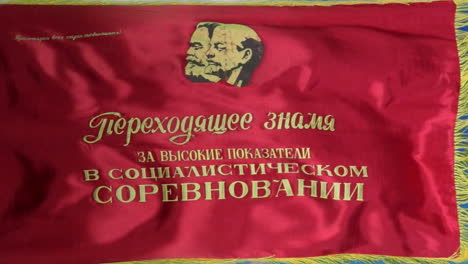 A-Soviet-flag-depicting-Marx-and-Lenin-with-the-caption,-"Transferrable-Banner-for-High-Results-in-Socialist-Competition"-flies-against-a-vivid-blue-sky
