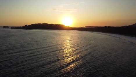Goldener-Sonnenuntergang-über-Dem-Ruhigen-Ozean-Mit-Silhouettierter-Küste